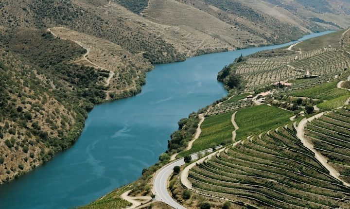 Statue overlooking a wide river valley with boats, green cliffs, and a bright cloudy sky
