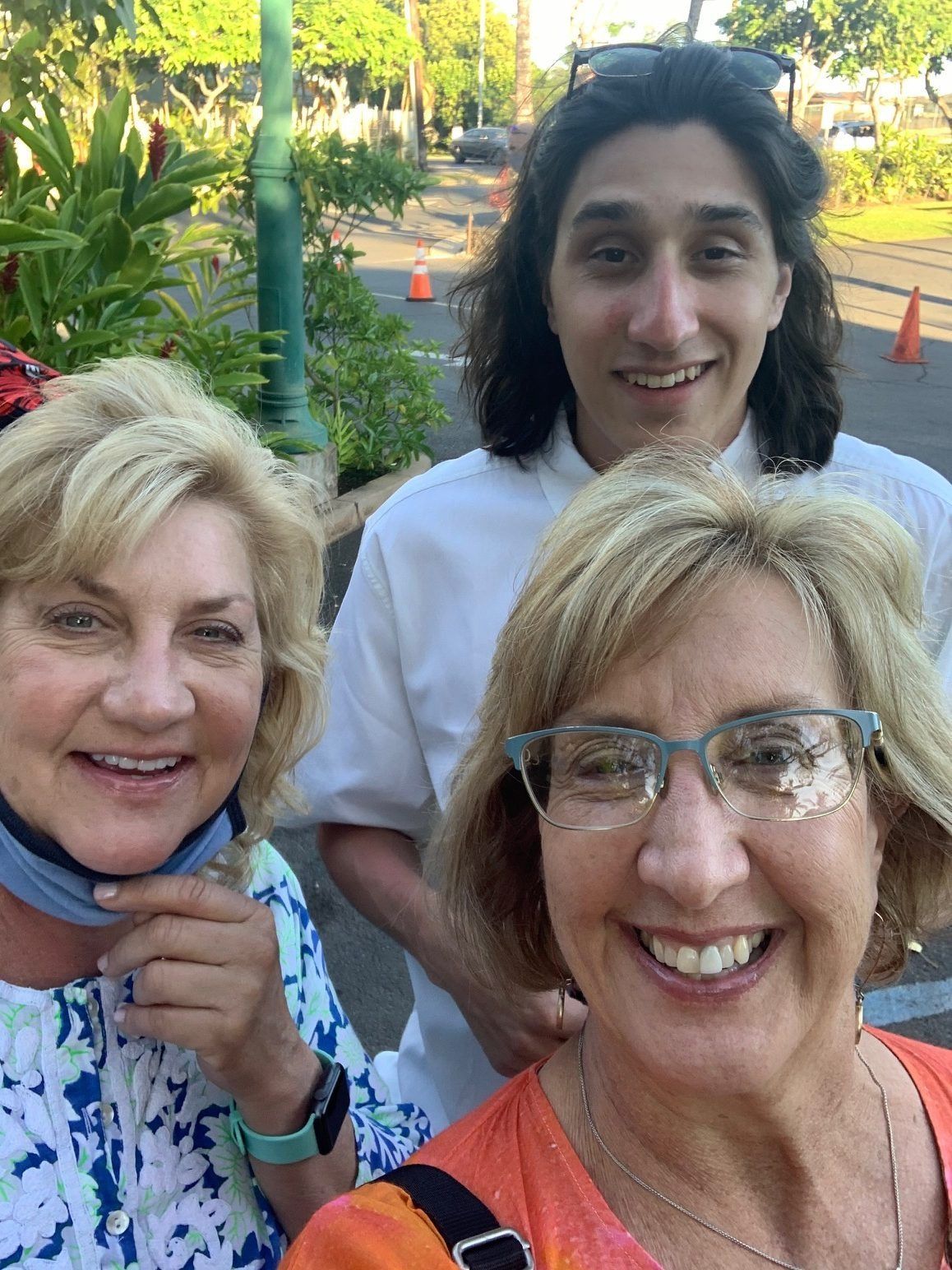 Three smiling people posing outdoors, with green trees and orange cones in the background.