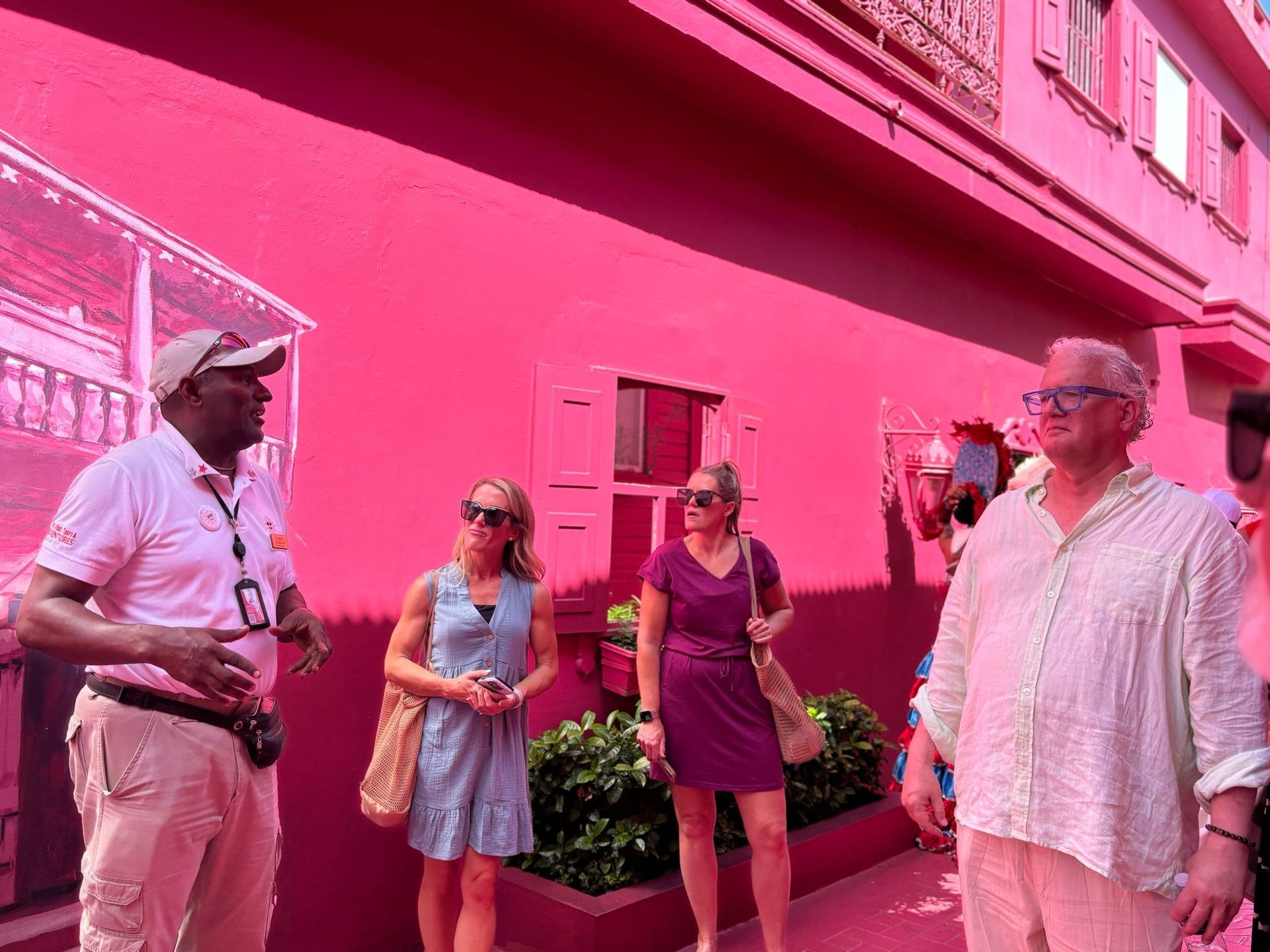 People standing outside a bright pink building, talking in a sunny courtyard