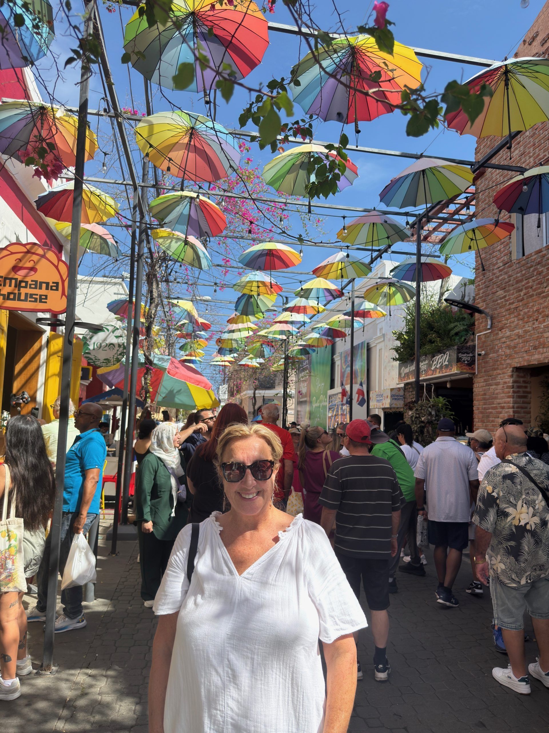 Crowded street festival with colorful umbrellas overhead and a woman in sunglasses walking in front