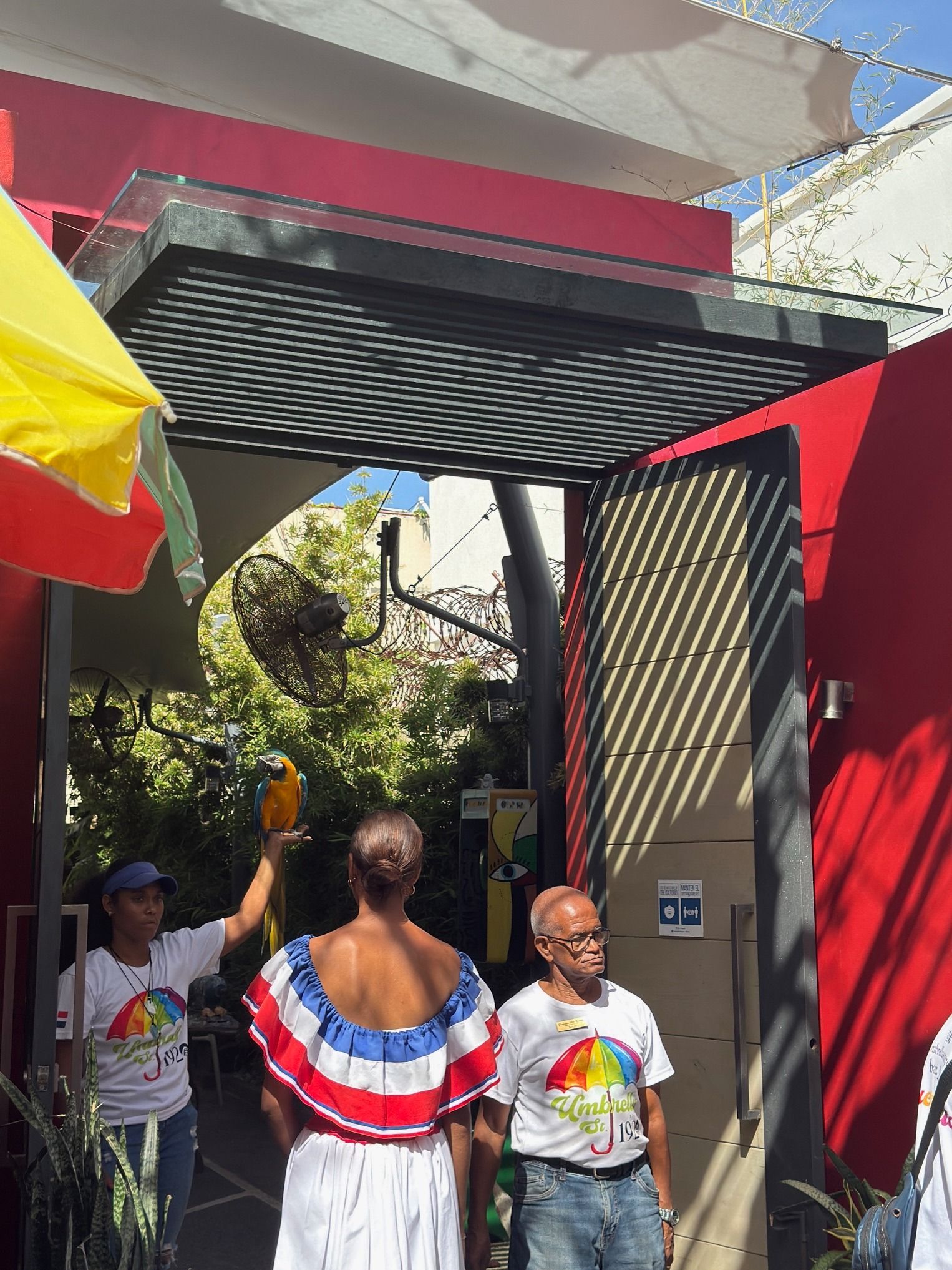 People standing at a colorful entrance gate with a black awning and red walls outdoors