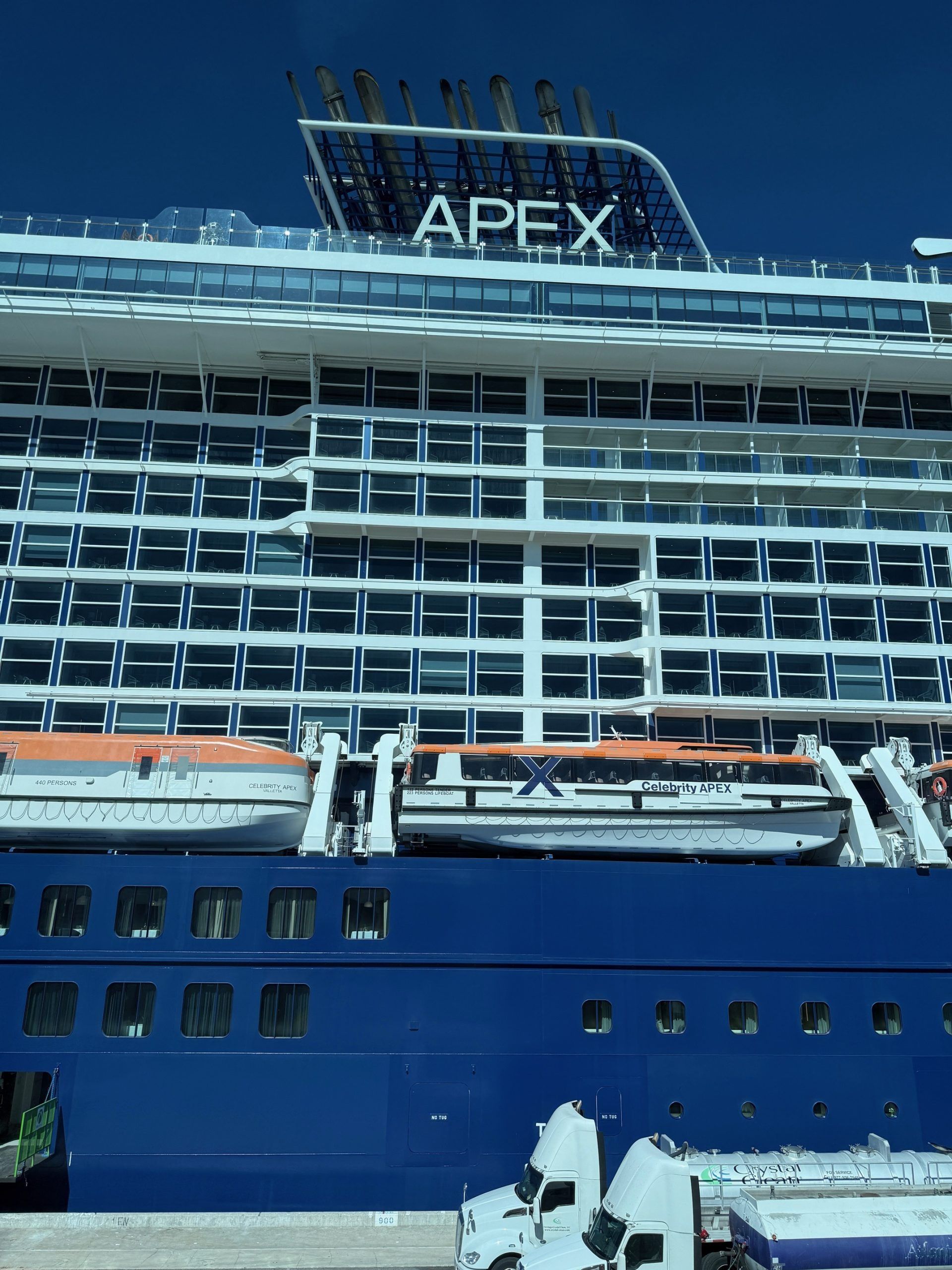Blue cruise ship docked with “APEX” sign on top, viewed from the side at port