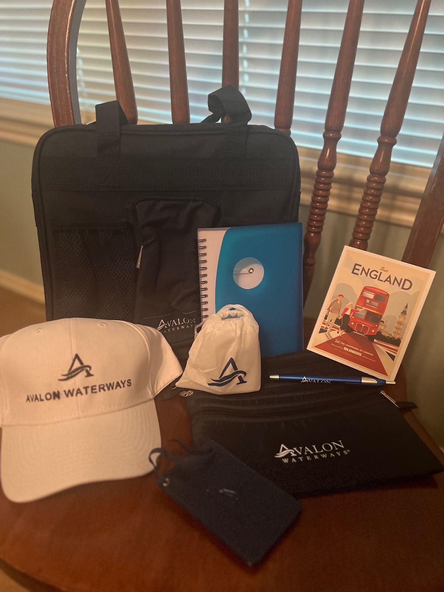 Promotional travel set with black backpack, white cap, pouch, notebook, pen, booklet, and blue card on a table.