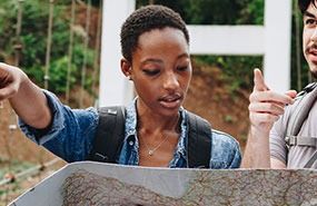 Two hikers studying a trail map outdoors, one pointing ahead.