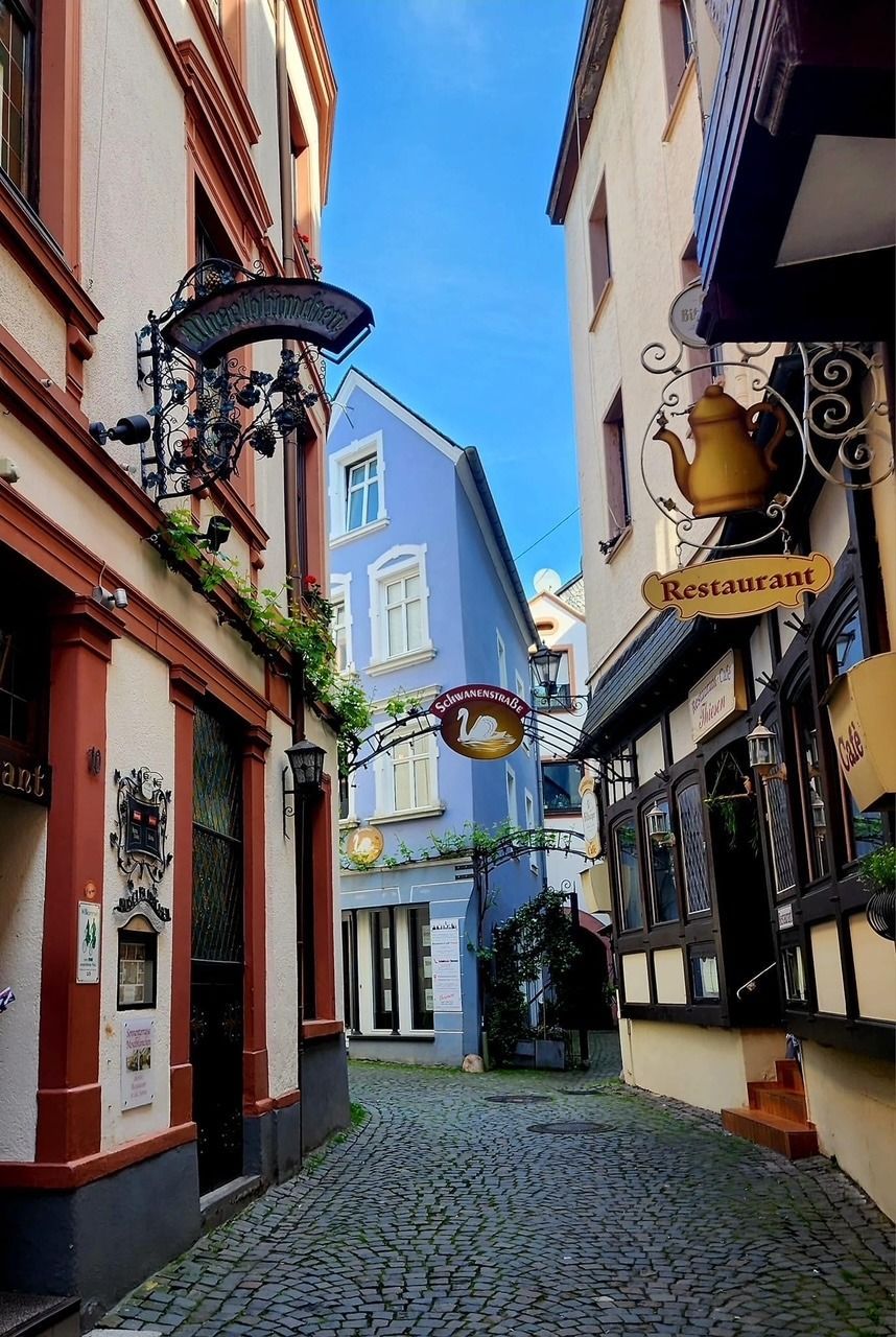Narrow cobblestone street with colorful buildings and hanging signs under a bright blue sky