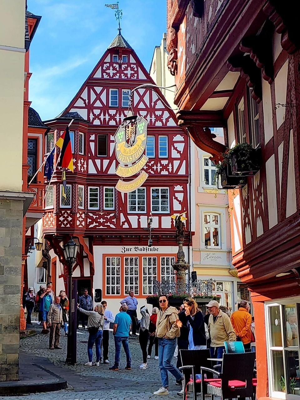 Crowded narrow street with half-timbered red-and-white buildings and people walking under signs