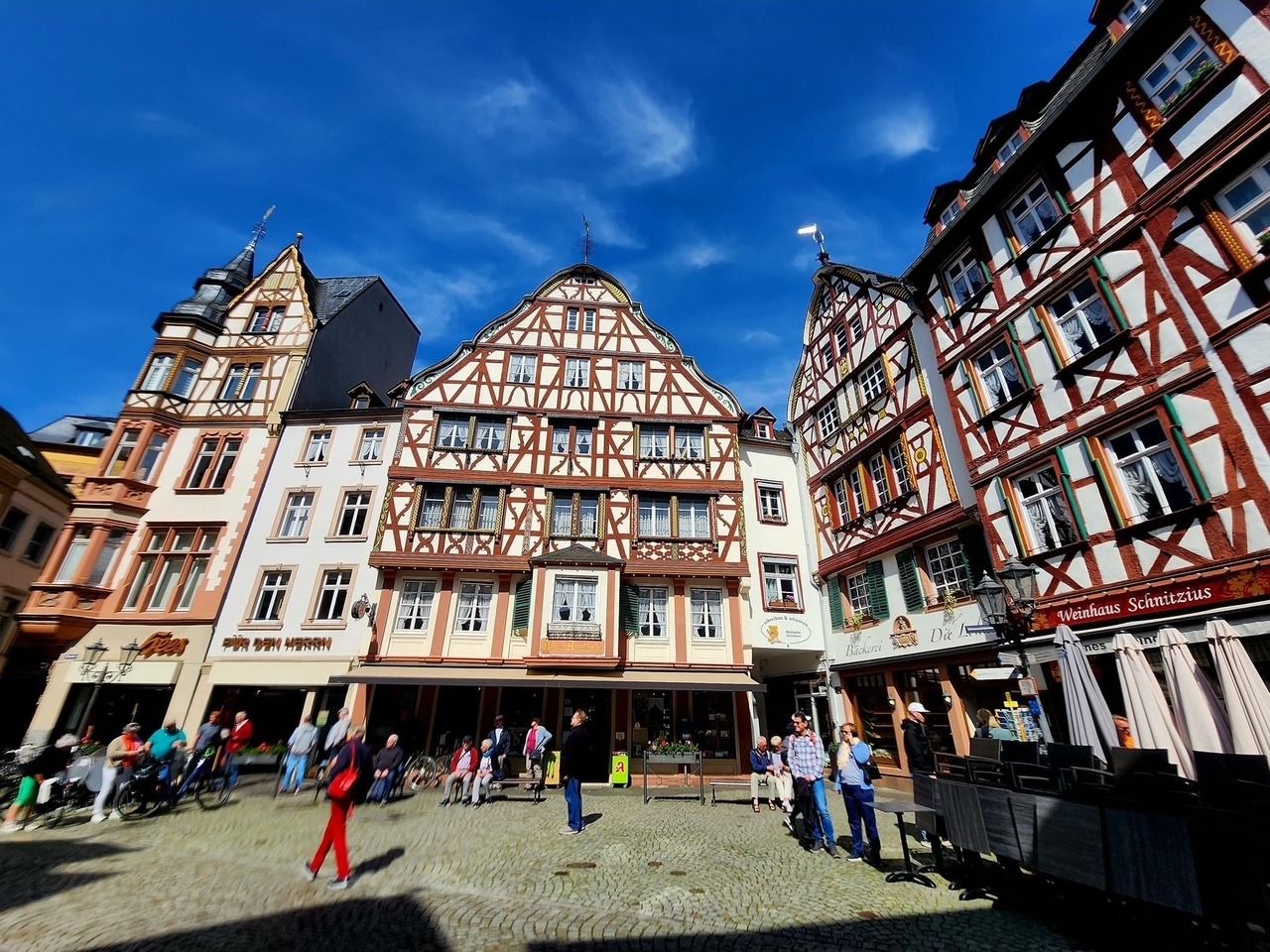 Historic half-timbered town square with people walking under a bright blue sky