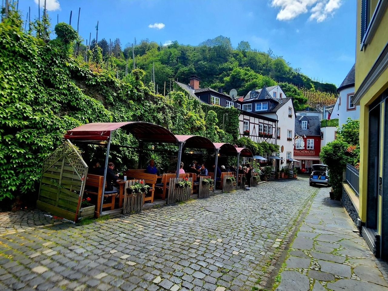 Cobblestone street with outdoor cafés and ivy-covered buildings in a small hillside village