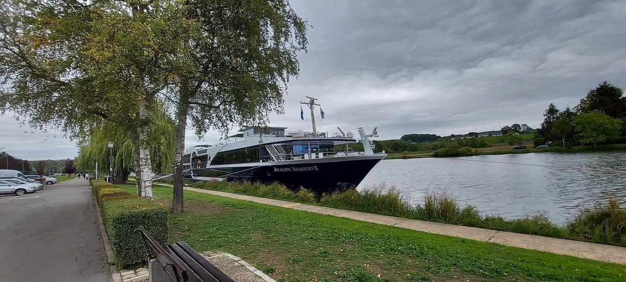 Large black yacht docked beside a riverside path on a cloudy day
