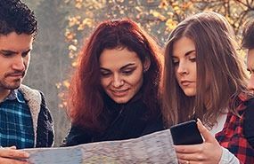 Three people outdoors looking at a map, smiling in warm sunlight.