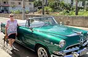 Person standing beside a green vintage convertible on a sunny street.