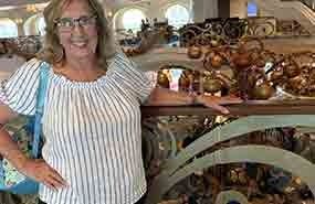 Woman in striped blouse stands beside shelves of decorative brown pottery in a shop.
