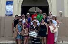 Group of people posing outside a beige building archway, many wearing sunglasses and summer clothes.