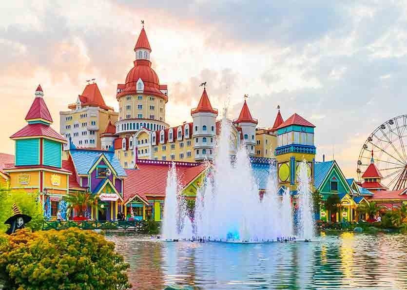 Colorful castle-style amusement park with fountain and lake under a bright sky
