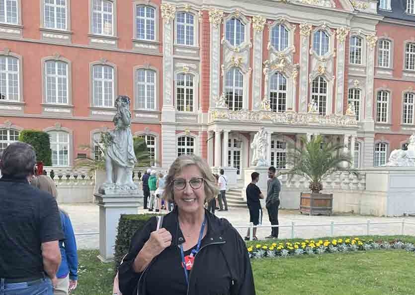 Woman smiling in a courtyard with a statue and ornate pink building in the background