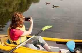Person in a yellow kayak photographing ducks on calm water.