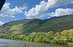 River beside green hillside under a cloudy blue sky