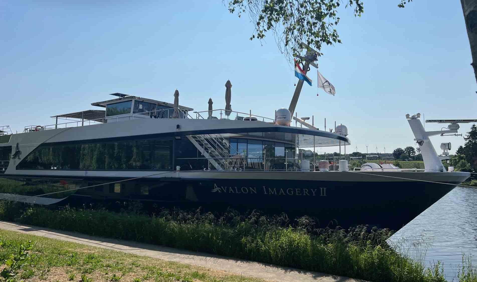 Large white yacht docked on a calm river under a clear blue sky, with flags flying above.