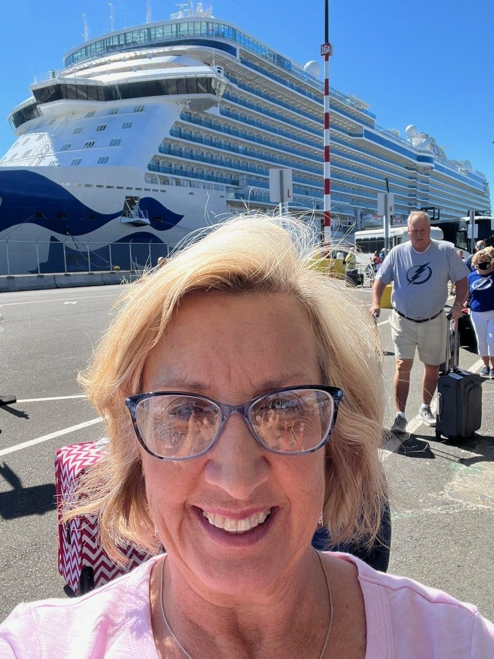 Smiling woman in glasses taking a selfie at a cruise ship dock.