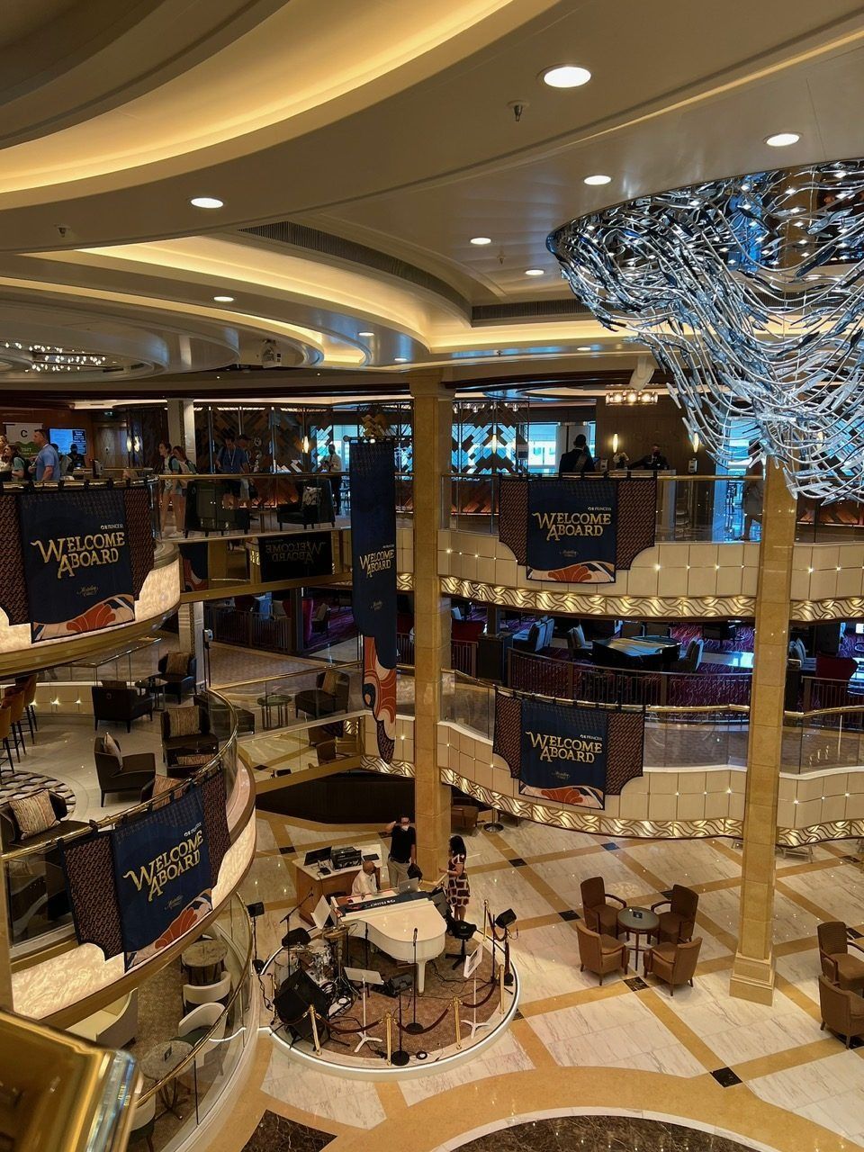Luxury hotel atrium with curved balconies, golden columns, and a large chandelier over a central seating area