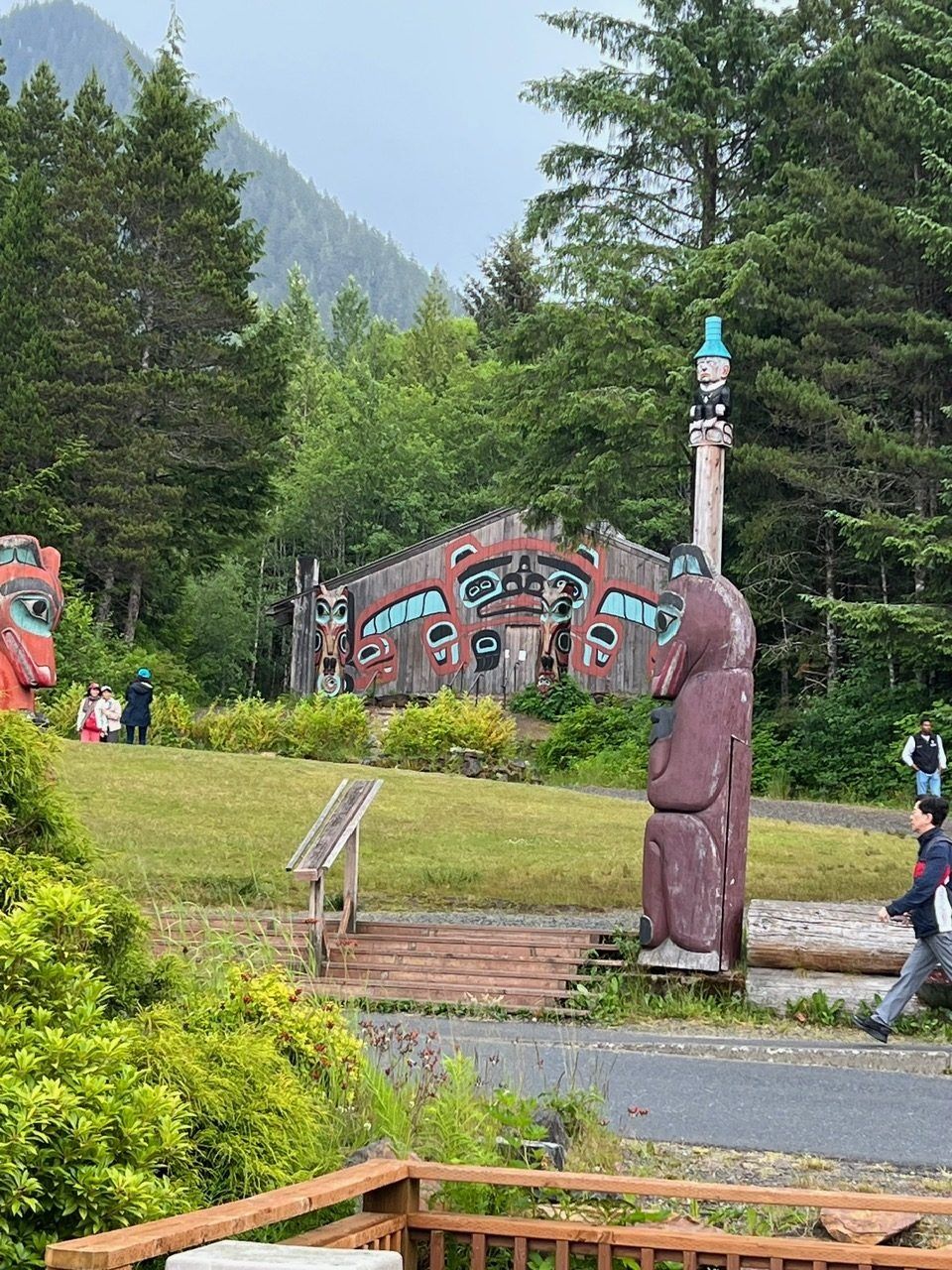 Totem poles in a grassy park with forested mountains in the background and a person walking nearby
