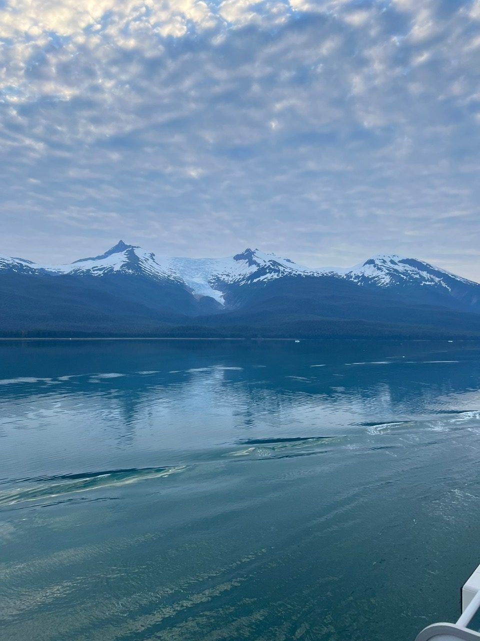 Snowy mountains reflected in a calm blue lake under a cloudy sky