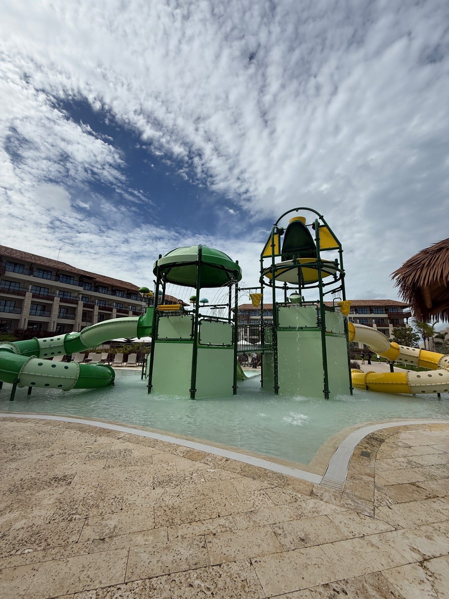 Colorful playground with green and yellow slides under a cloudy sky, surrounded by buildings