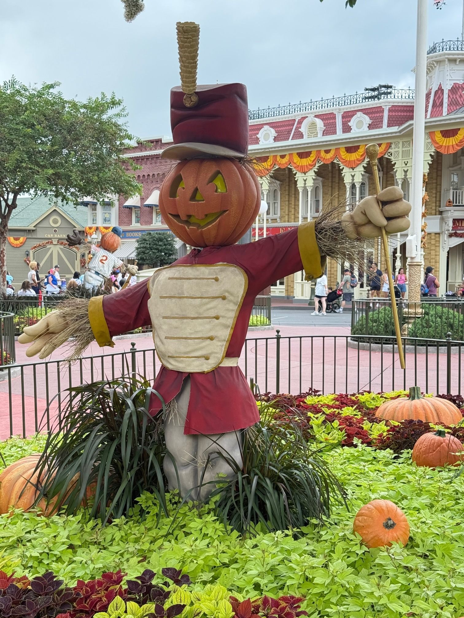 Scarecrow with pumpkin head and raised arms in a flower bed at a festive autumn display
