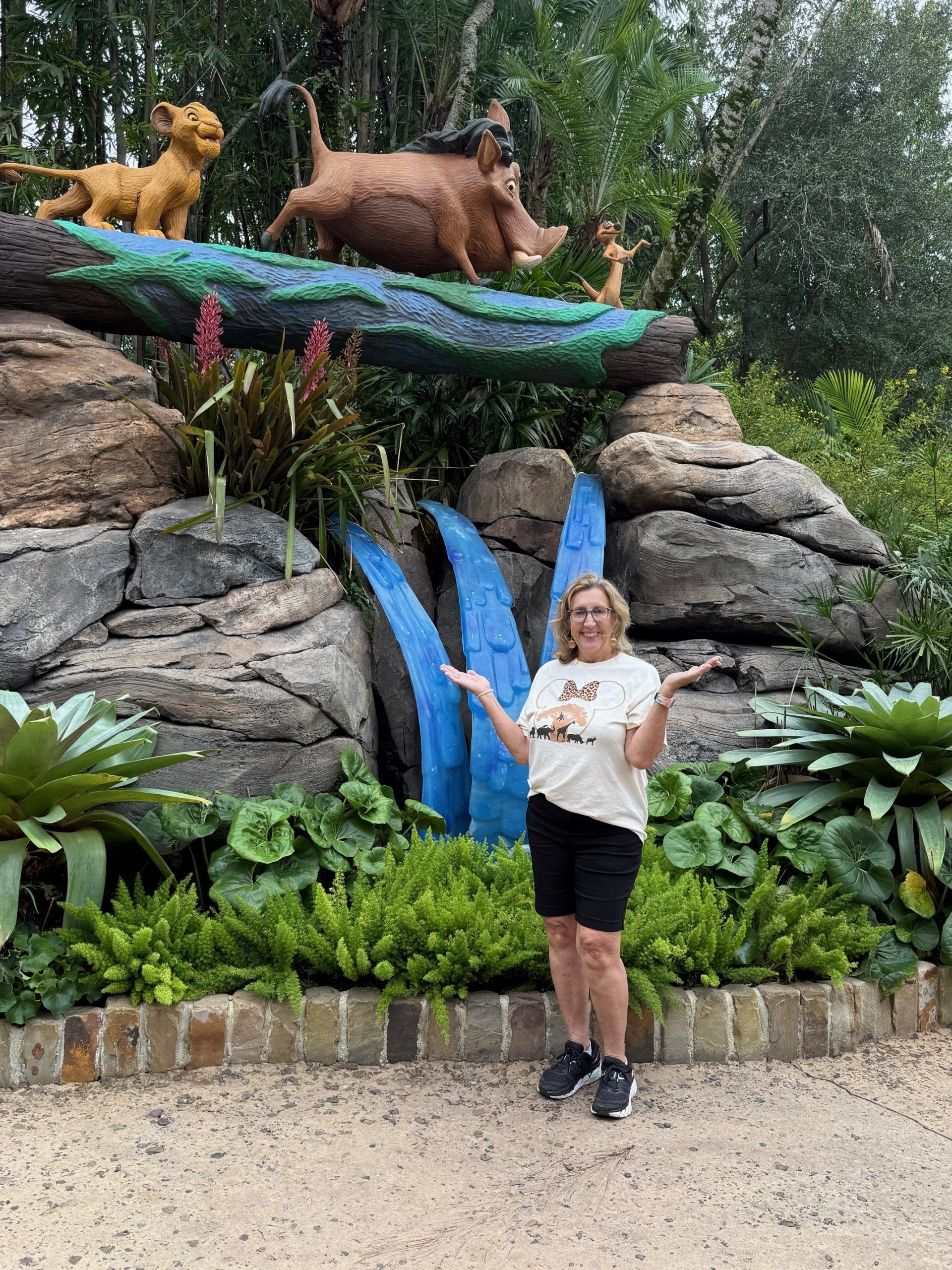 Woman posing beside jungle-themed waterfall display with animal sculptures and lush greenery