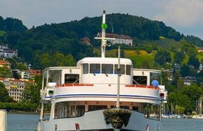 White passenger boat on a lake with green hills and lakeside buildings in the background