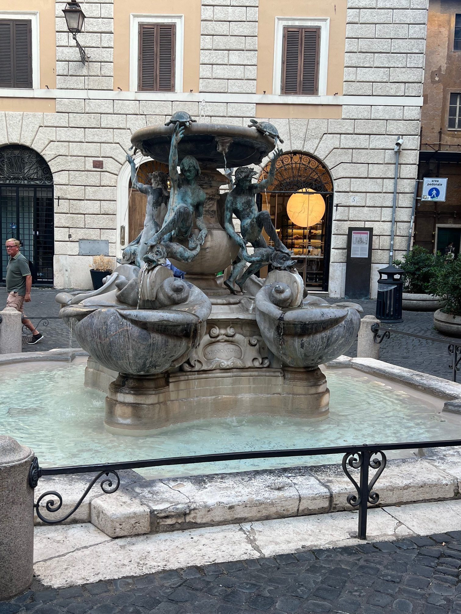 Stone fountain in a courtyard, with sculpted figures and water in front of a historic building.