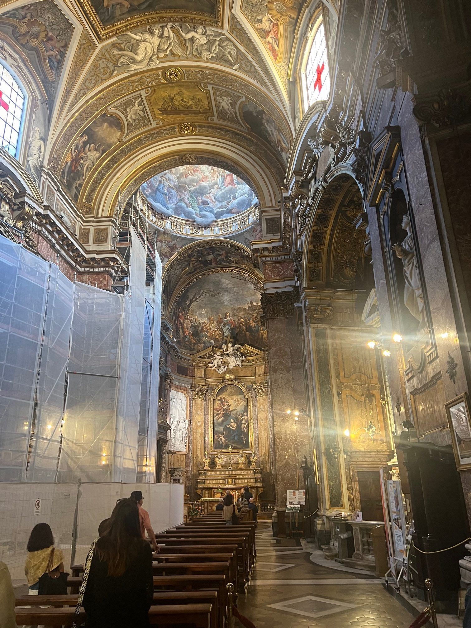 Ornate gilded church interior with vaulted ceiling, rows of pews, and a few visitors near the entrance