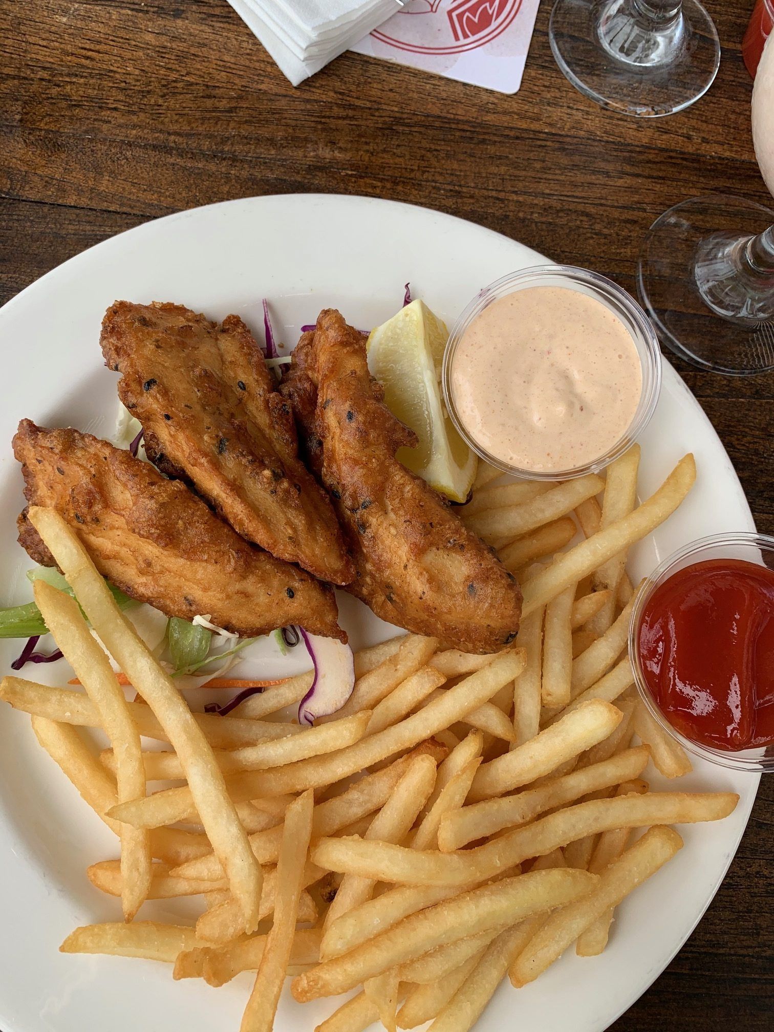 Plate of fried fish strips and French fries with lemon wedge, tartar sauce, ketchup, and red onion slices