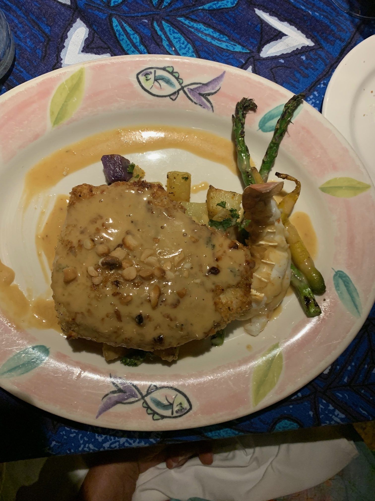 Plate of creamy sauce-covered food with asparagus on a floral dish, set on a blue tablecloth.