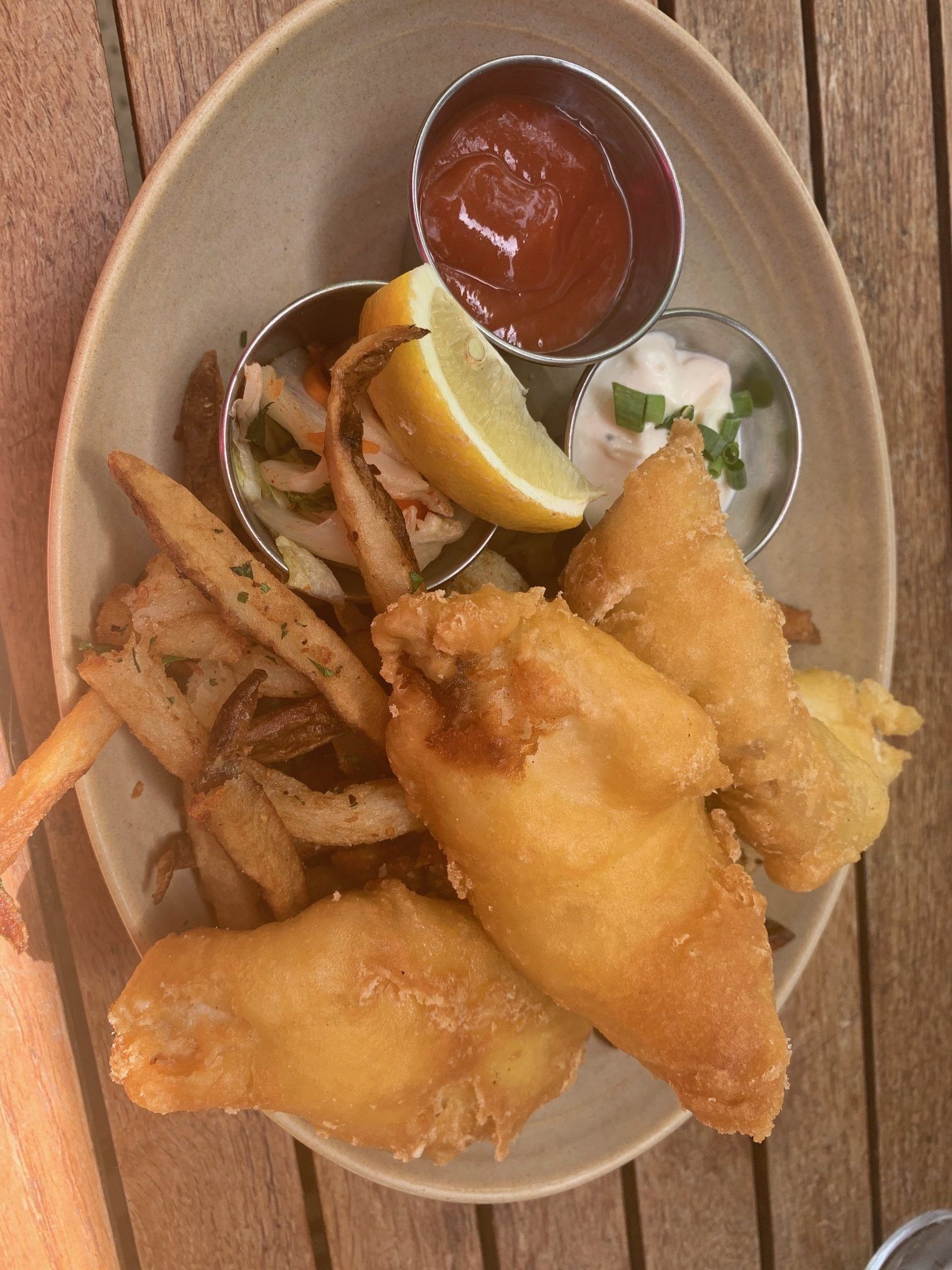 Fried fish and chips with fries, lemon wedge, coleslaw, and dipping sauce in a basket