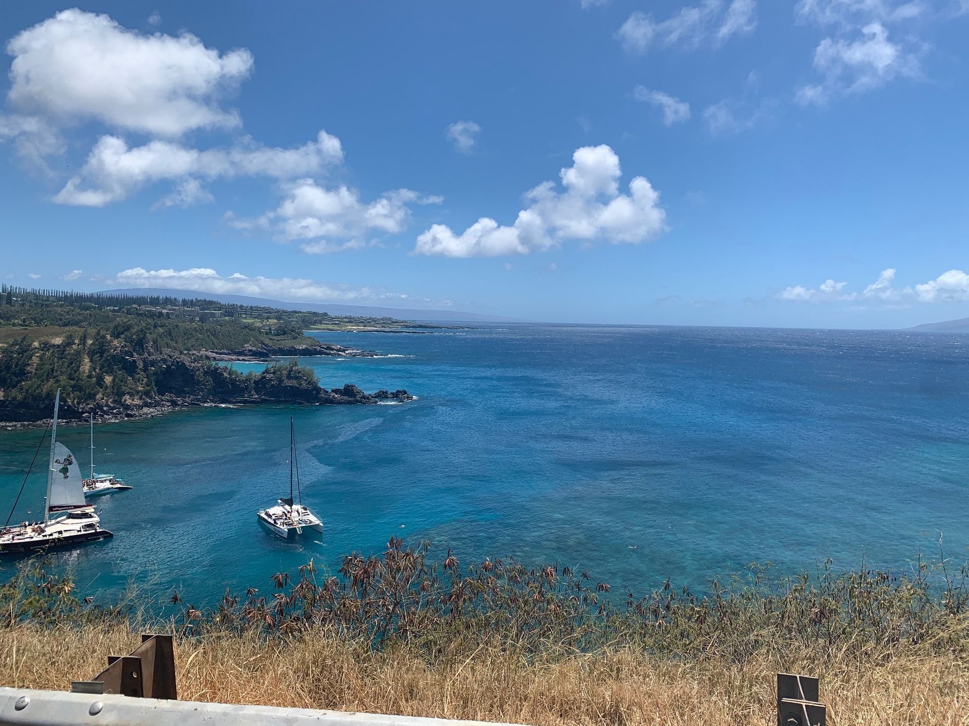 Coastal bay with blue ocean, small boats, rocky shoreline, and a partly cloudy sky