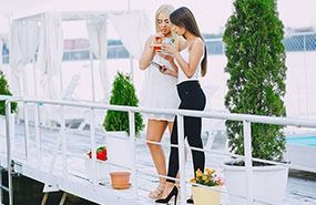 Two people sharing a drink on a white balcony with potted plants