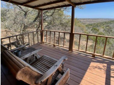 Wooden porch with rustic chair overlooking a wooded landscape under a covered roof