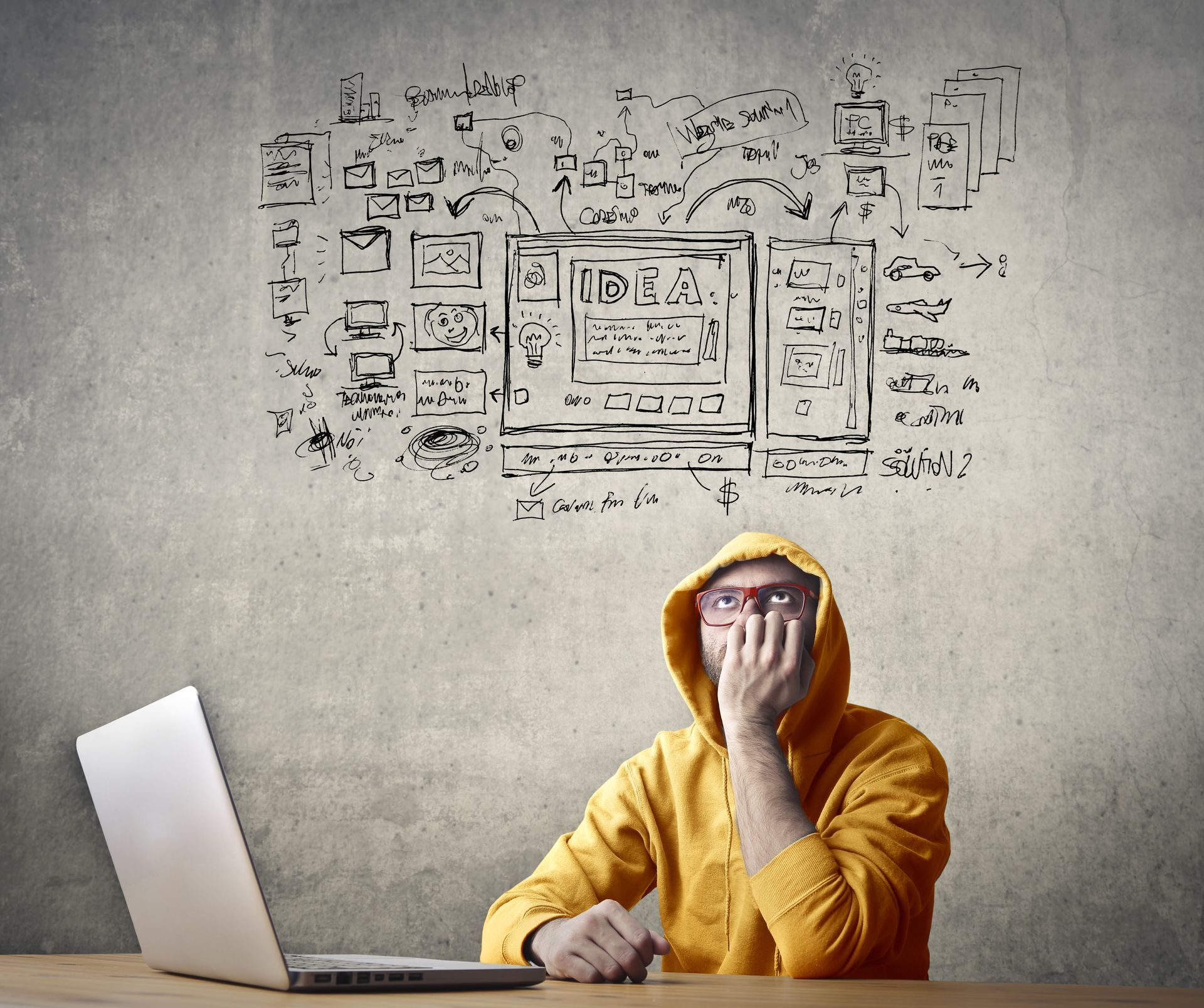 A man in a yellow hoodie is sitting at a desk with a laptop