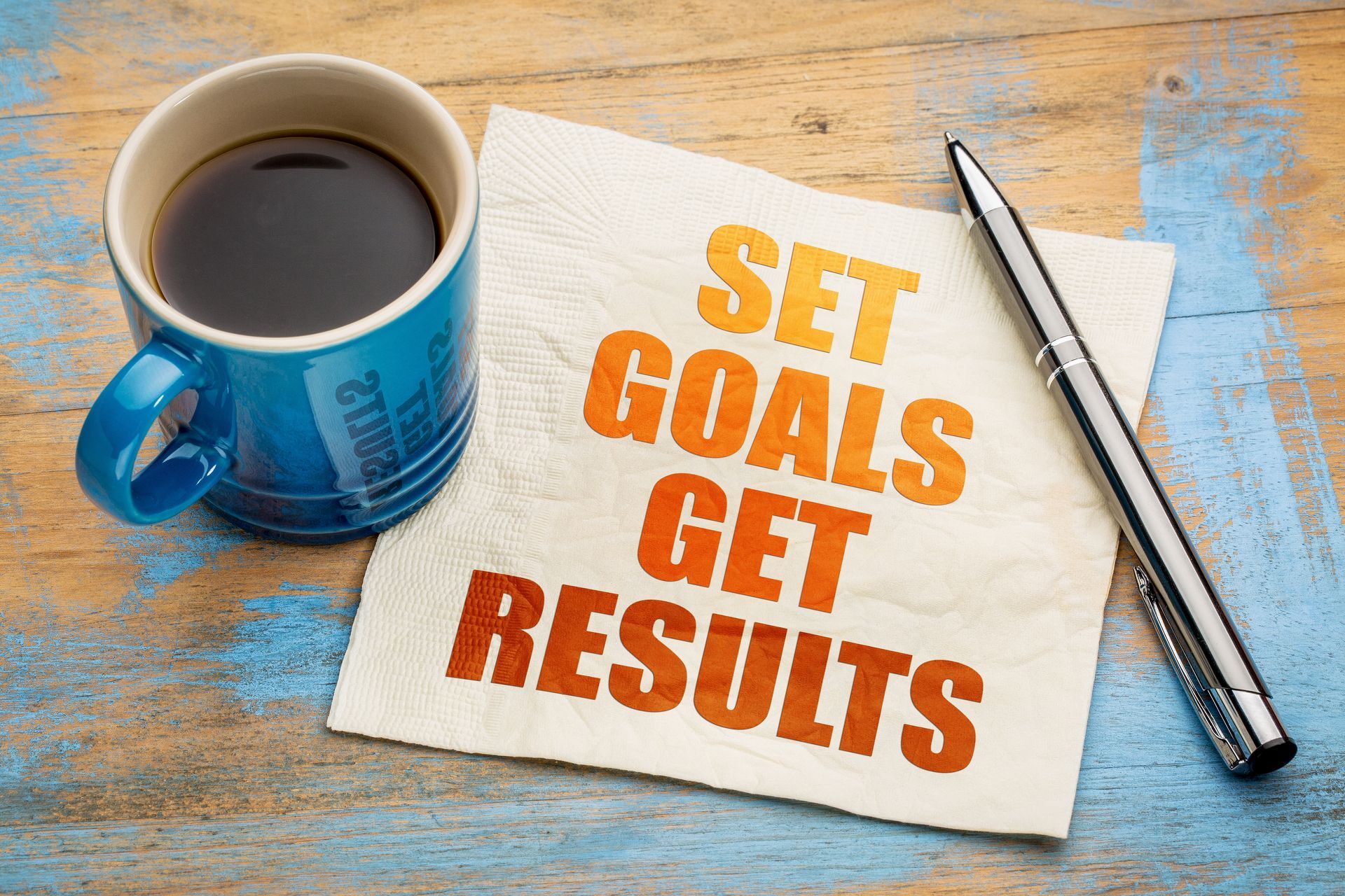 A napkin with the words `` set goals get results '' next to a cup of coffee and a pen.