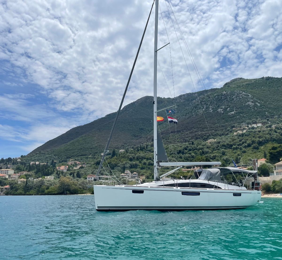 White sailboat on turquoise water with a green mountainside and cloudy sky in the background