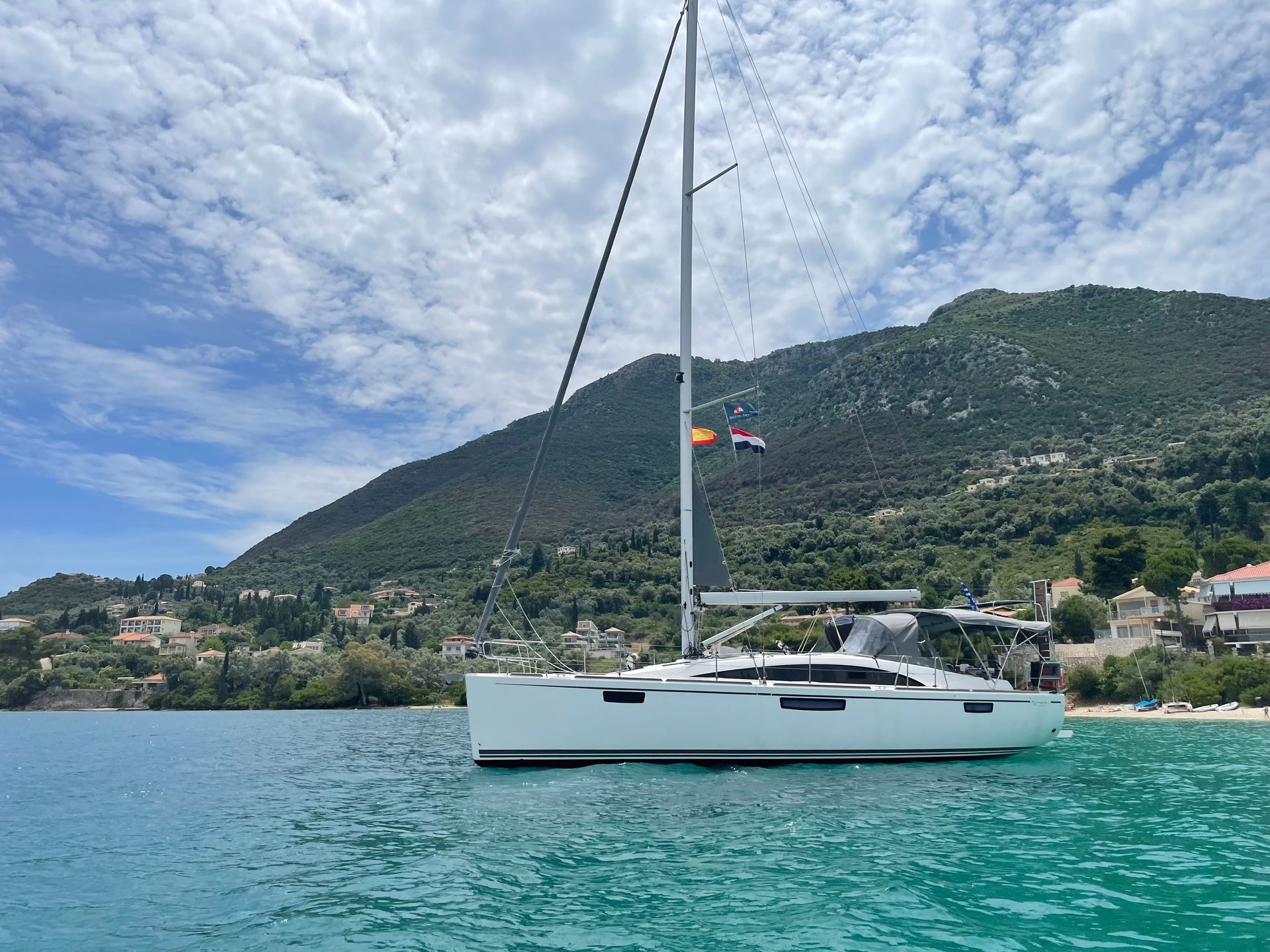 White sailboat on turquoise water with a green hillside and cloudy sky in the background