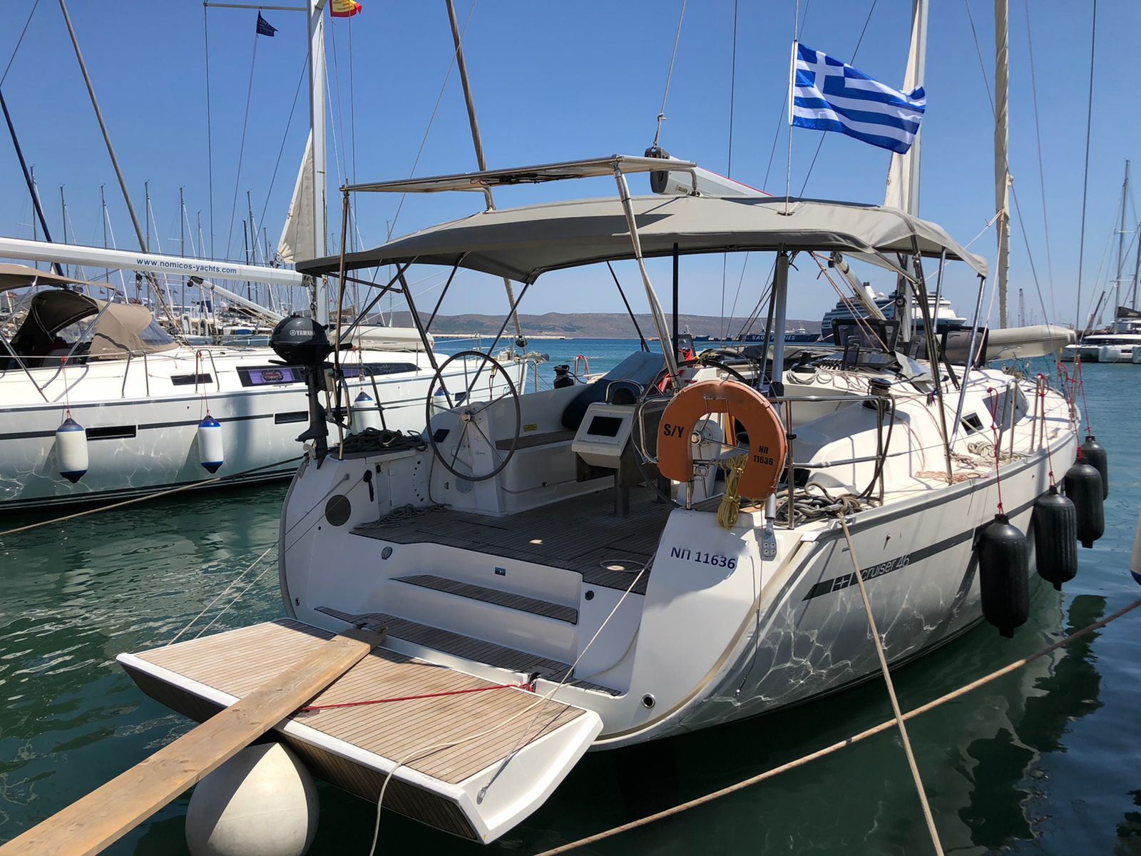 Sailboat docked at a marina, with Greek flag and calm blue water.