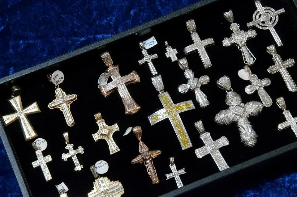 Assorted silver and gold cross pendants displayed in a black tray on a blue background