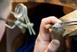 Hands working with pliers on a small metal piece near a tool bench