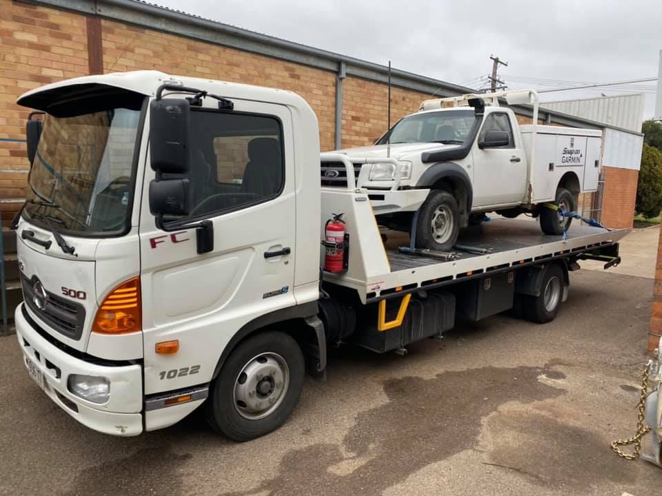 A Tow Truck with Two Cars on The Back Is Parked in Front of A Brick Building — Multidrive Parts Australia in Taminda, NSW