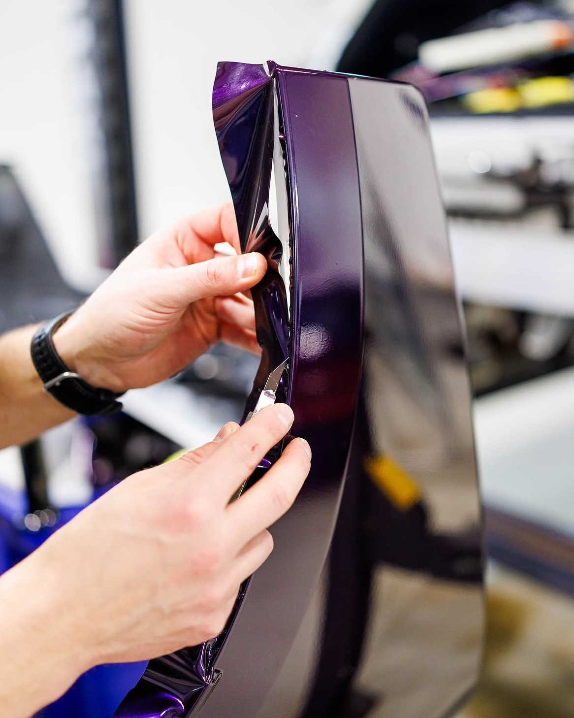 Hands applying glossy purple vinyl film to a curved panel in a workshop
