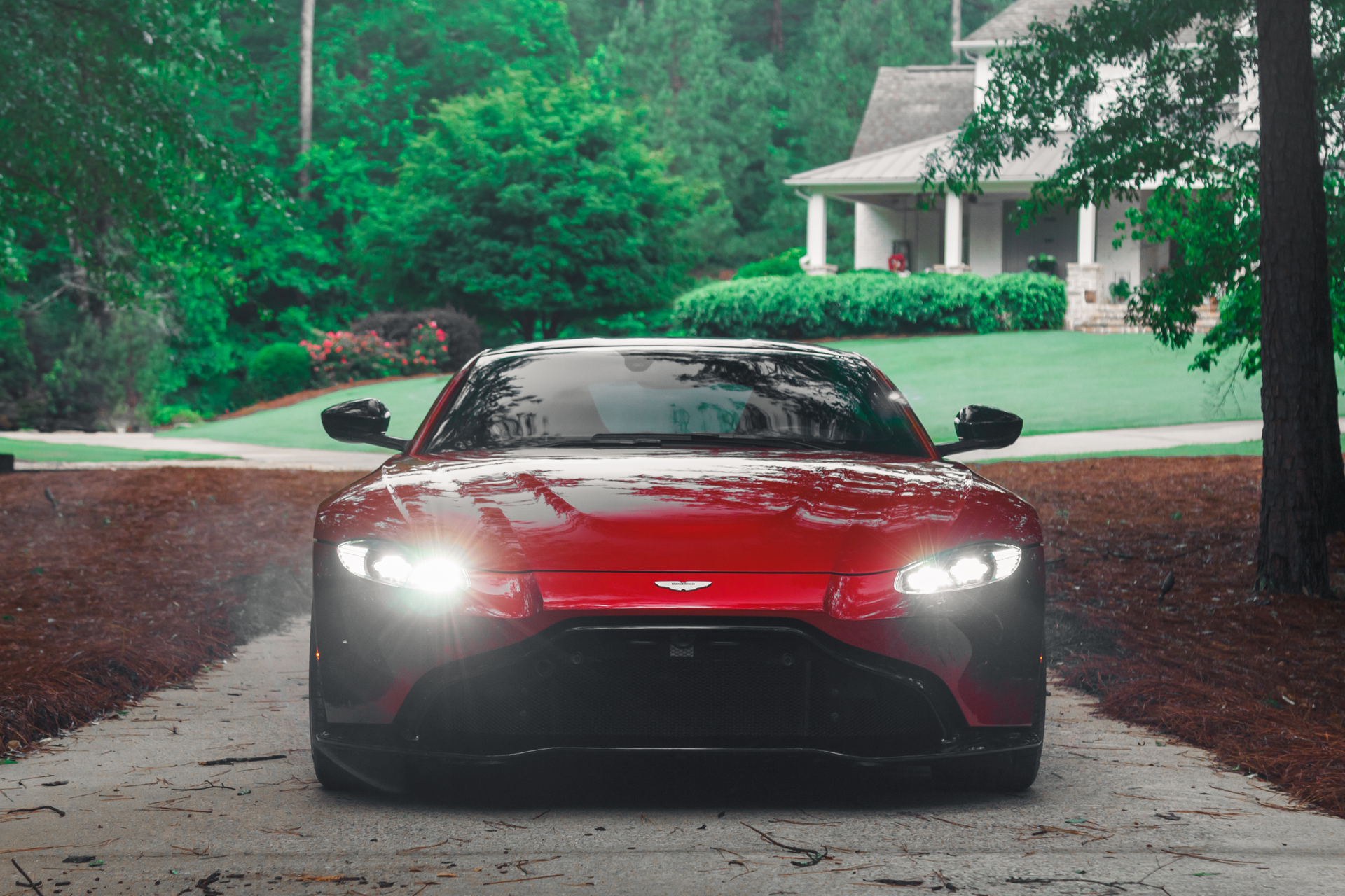 Red sports car on a tree-lined driveway in front of a house