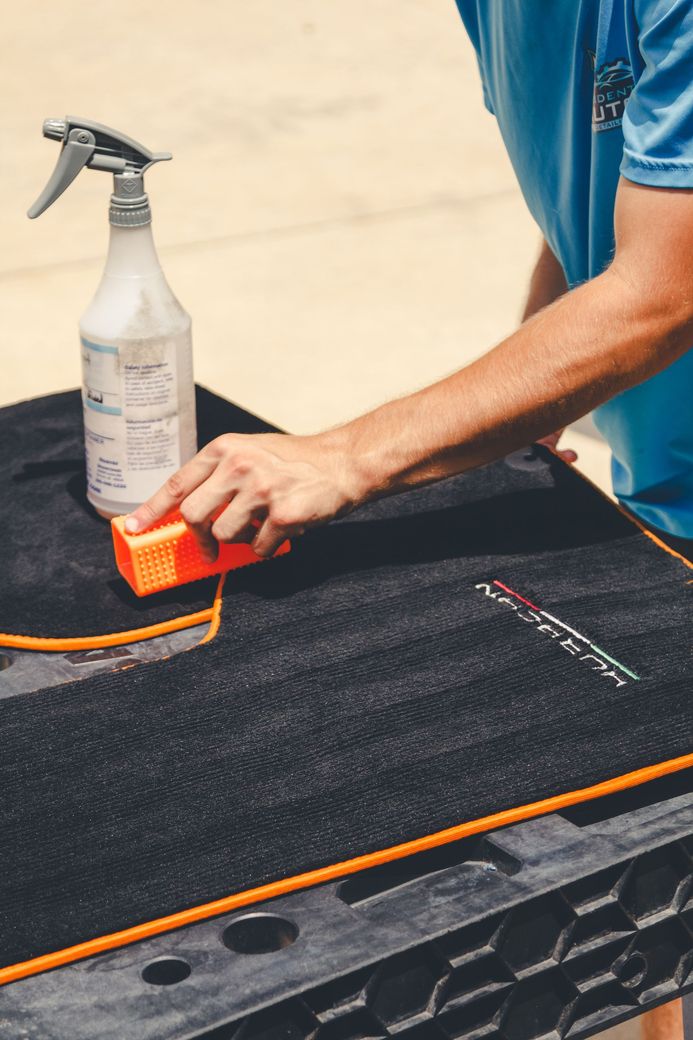 Person cleaning a black textured surface with an orange sponge beside a spray bottle
