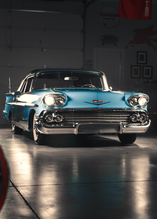 Classic turquoise 1950s Chevrolet in a garage, front view with chrome details and glossy reflections on the floor